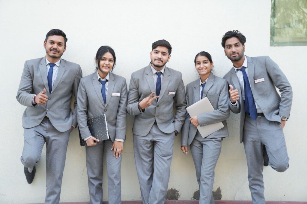 Group of young professionals in formal suits posing with smiles and confidence against a wall.