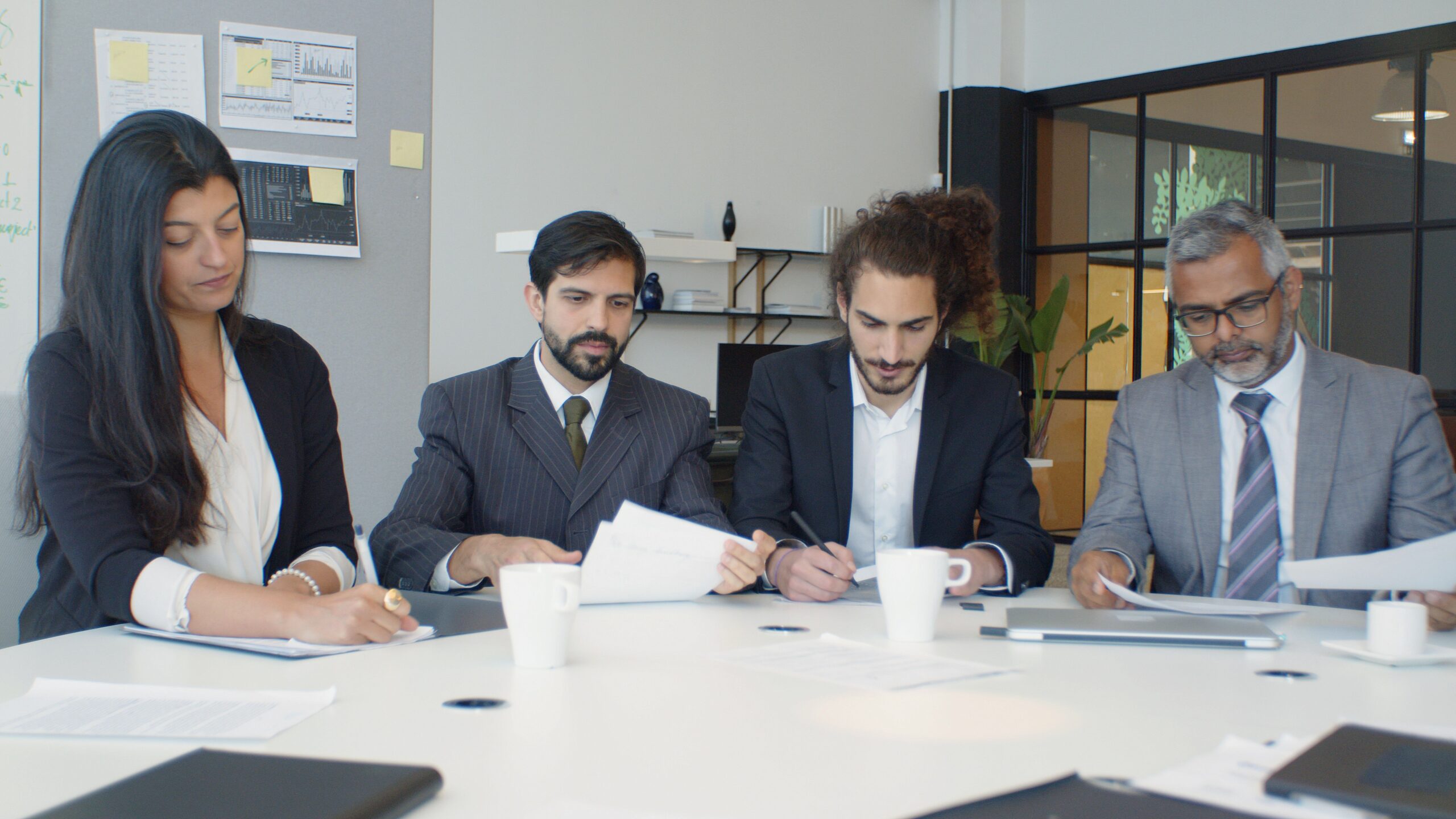 Group of business professionals engaged in a team meeting around a desk in a modern office setting.